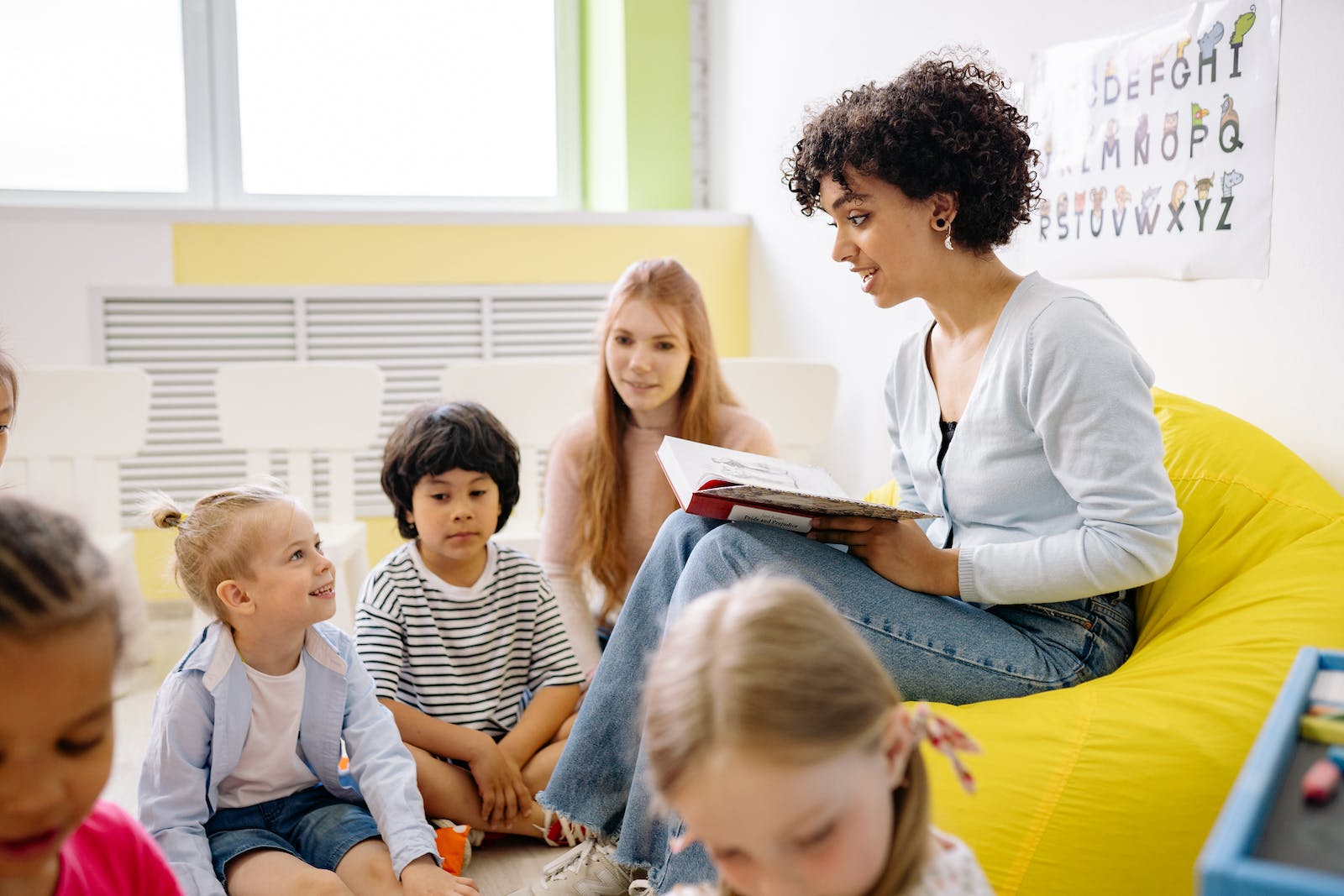 Educatrice petite enfance lisant une histoire à un groupe de petits, dans une salle éclairée
